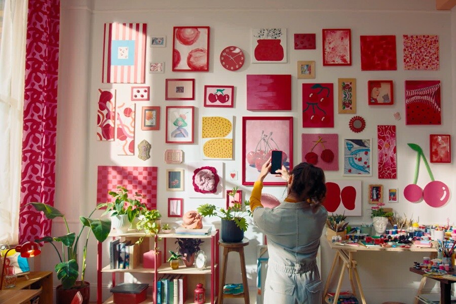 Salon z obrazami o tematyce wiśni zawieszonymi za pomocą rzepów Command, a także półką z książkami i roślinami oraz stołem z materiałami plastycznymi.
